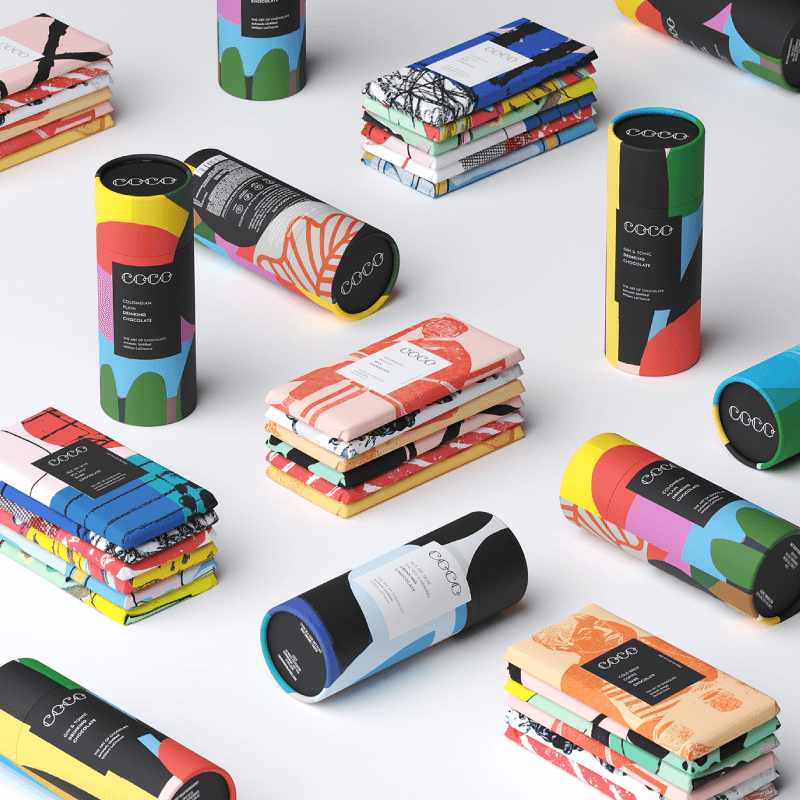 A variety of colorful COCO brand chocolate bars and cylindrical packages are neatly arranged on a white surface.